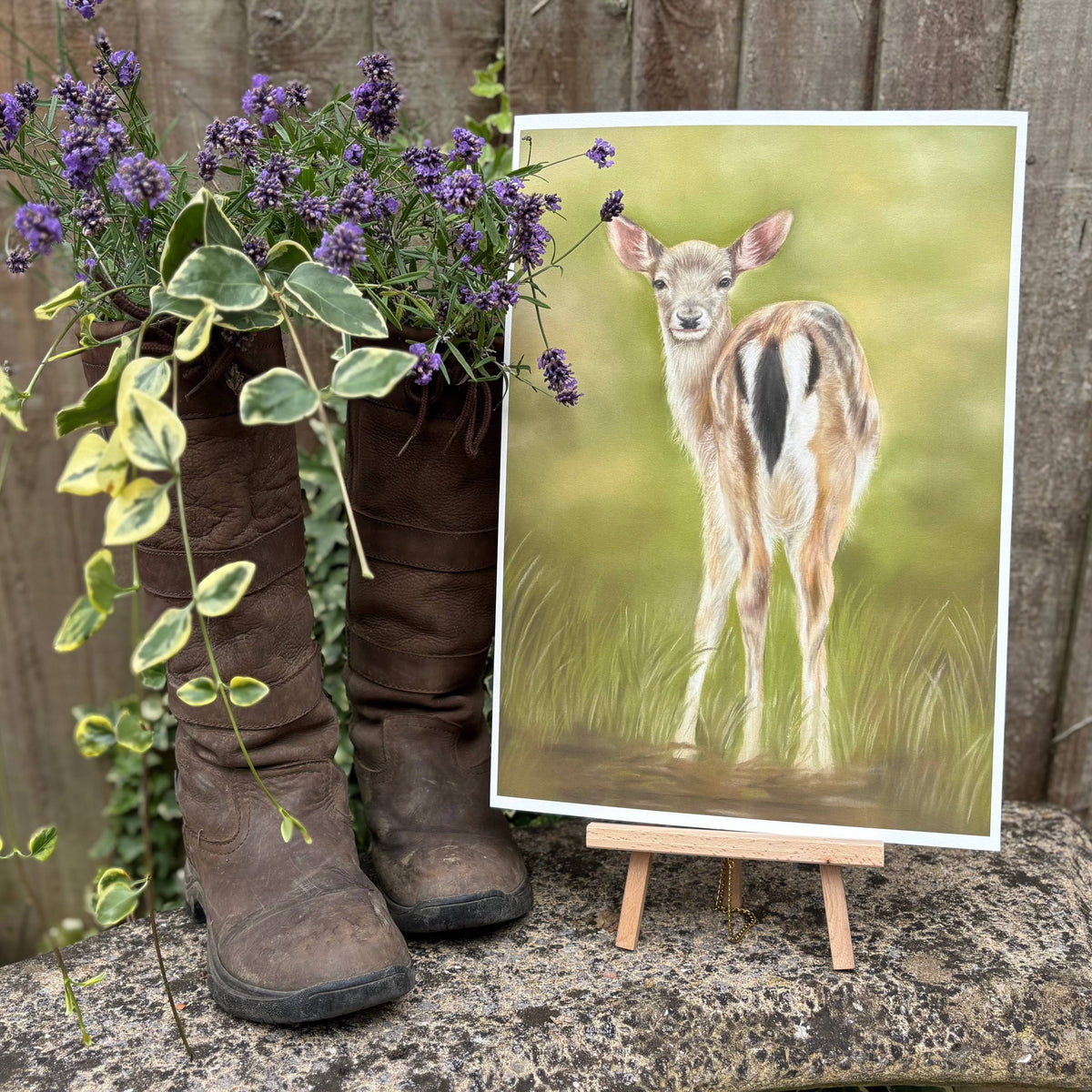 Fallow Fawn Fine Art Print On Paper on a mini easel outdoors, styled with vintage boots and lavender, evoking a countryside garden feel.
