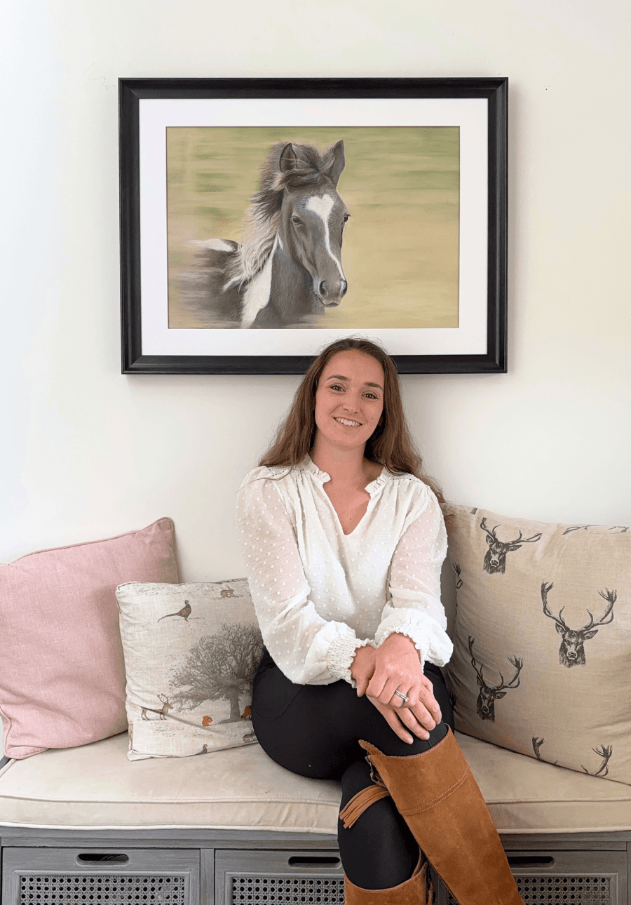 Equestrian original painting 'Flying Free' by Georgie Turner shown framed above a bench with a woman seated, perfect for rustic interior styling.