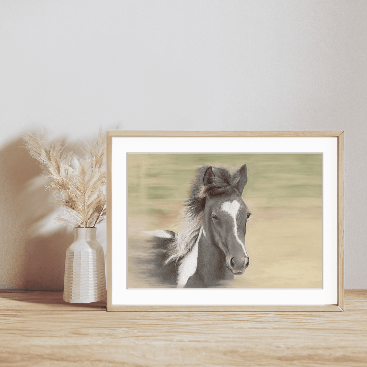 Galloping Foal Fine Art Print displayed in a light wood frame on a wooden shelf with a neutral vase, ideal for equestrian-themed home decor.