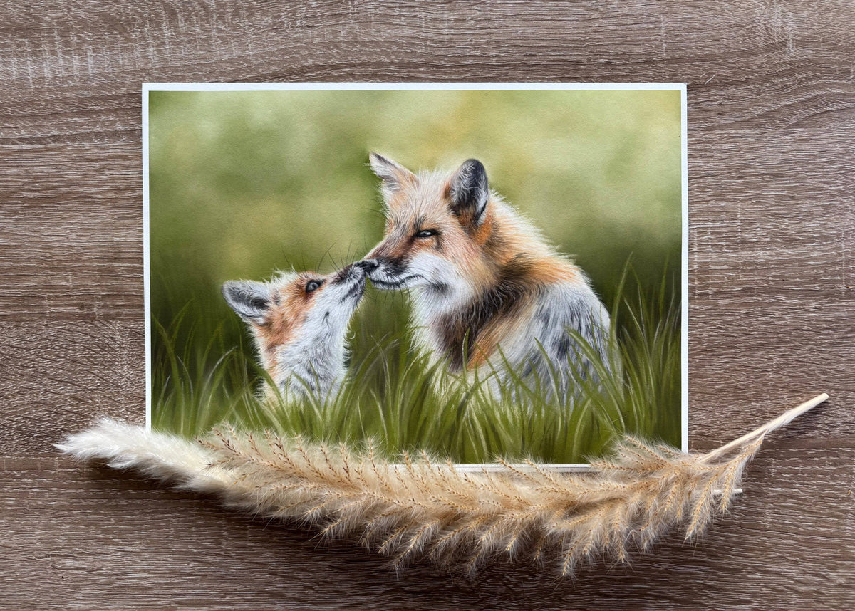 Fox & Cub Fine Art Print On Paper laid flat on wooden surface with pampas grass, showcasing wildlife art for home decoration.