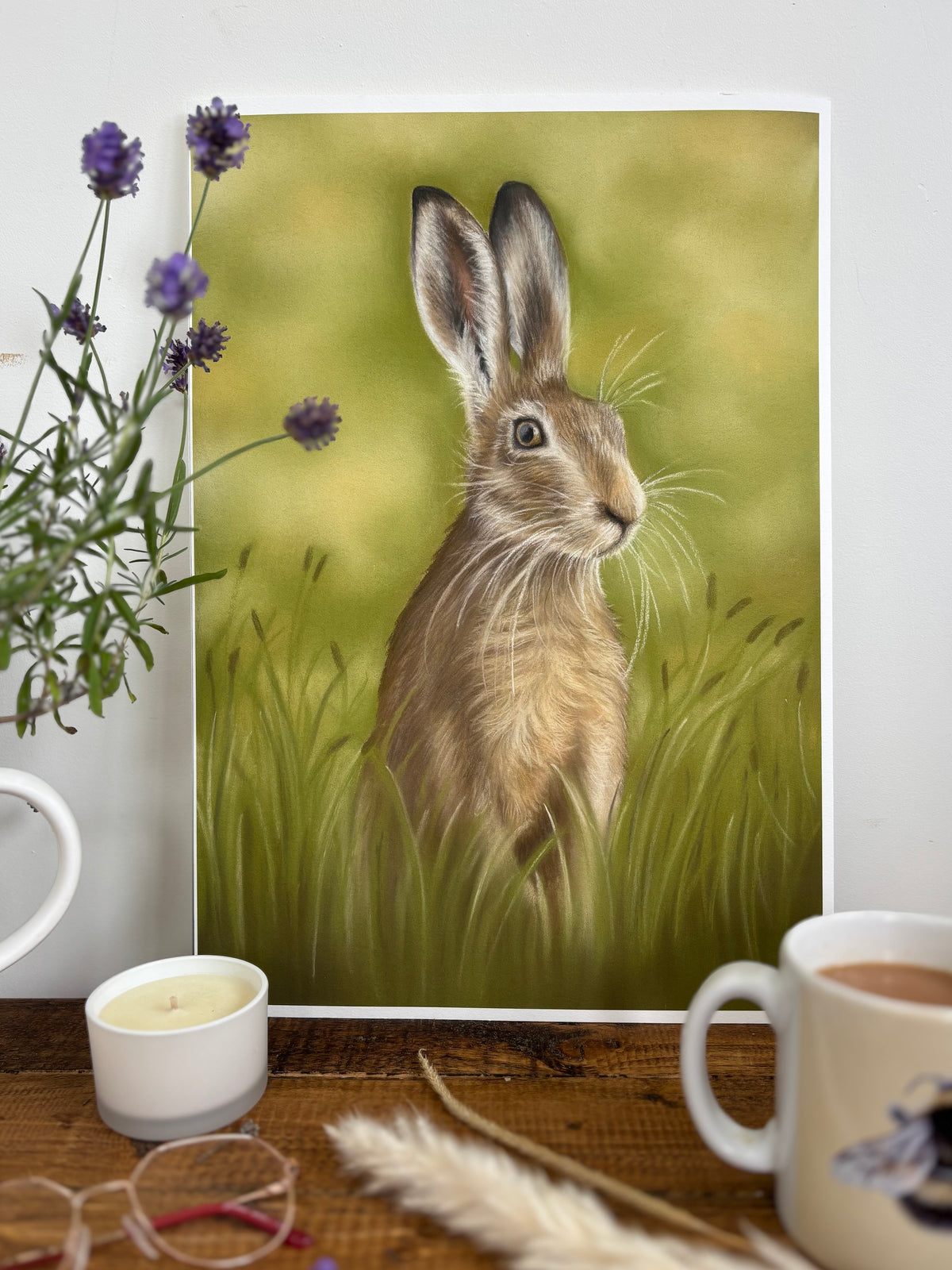 Hare In The Grass Fine Art Print On Paper styled with tea, candle, and flowers, enhancing cozy British countryside interior design.