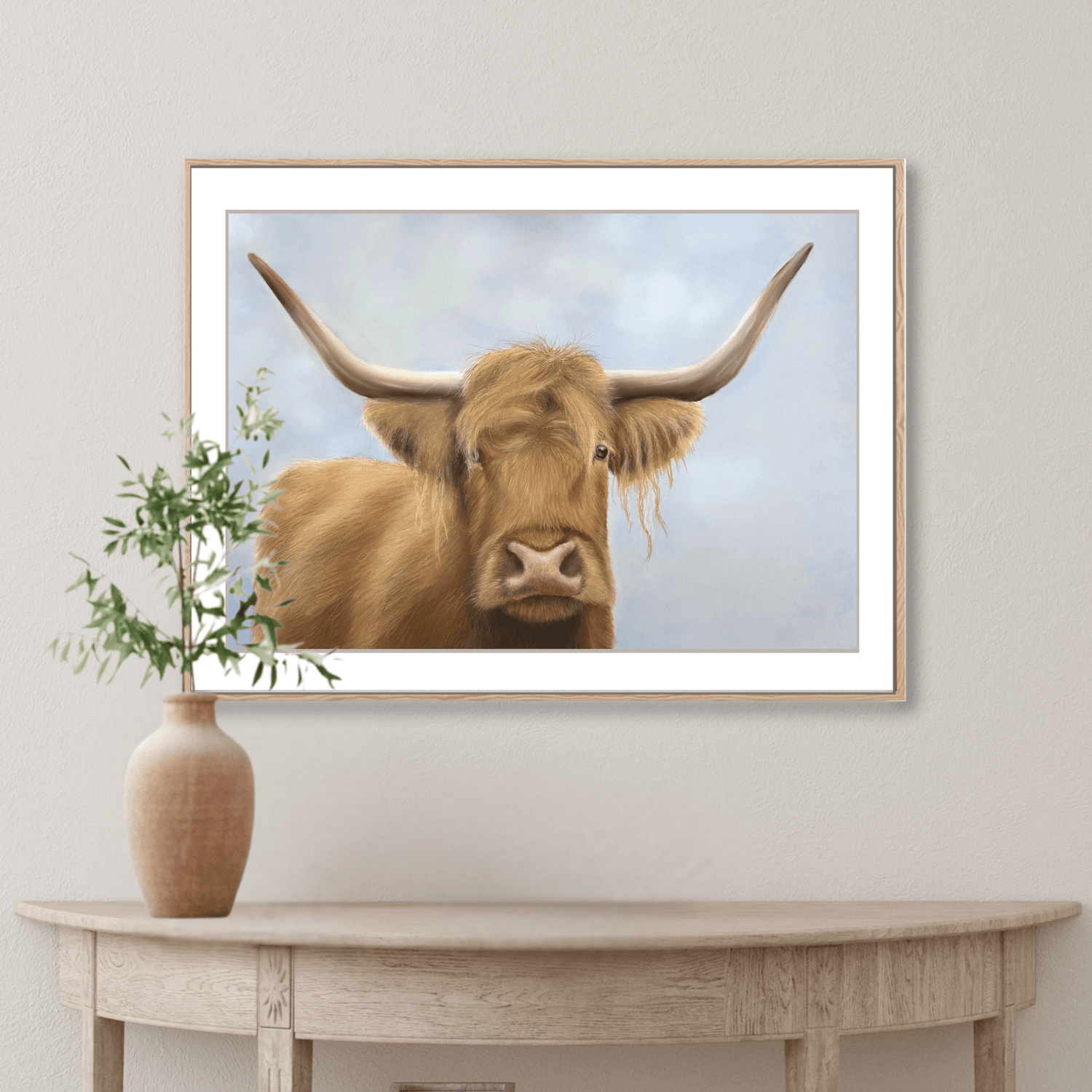 Framed Scottish Highland Cow Print hanging above a wooden console table with ceramic vase. Country-style wall art for farmhouse interiors.