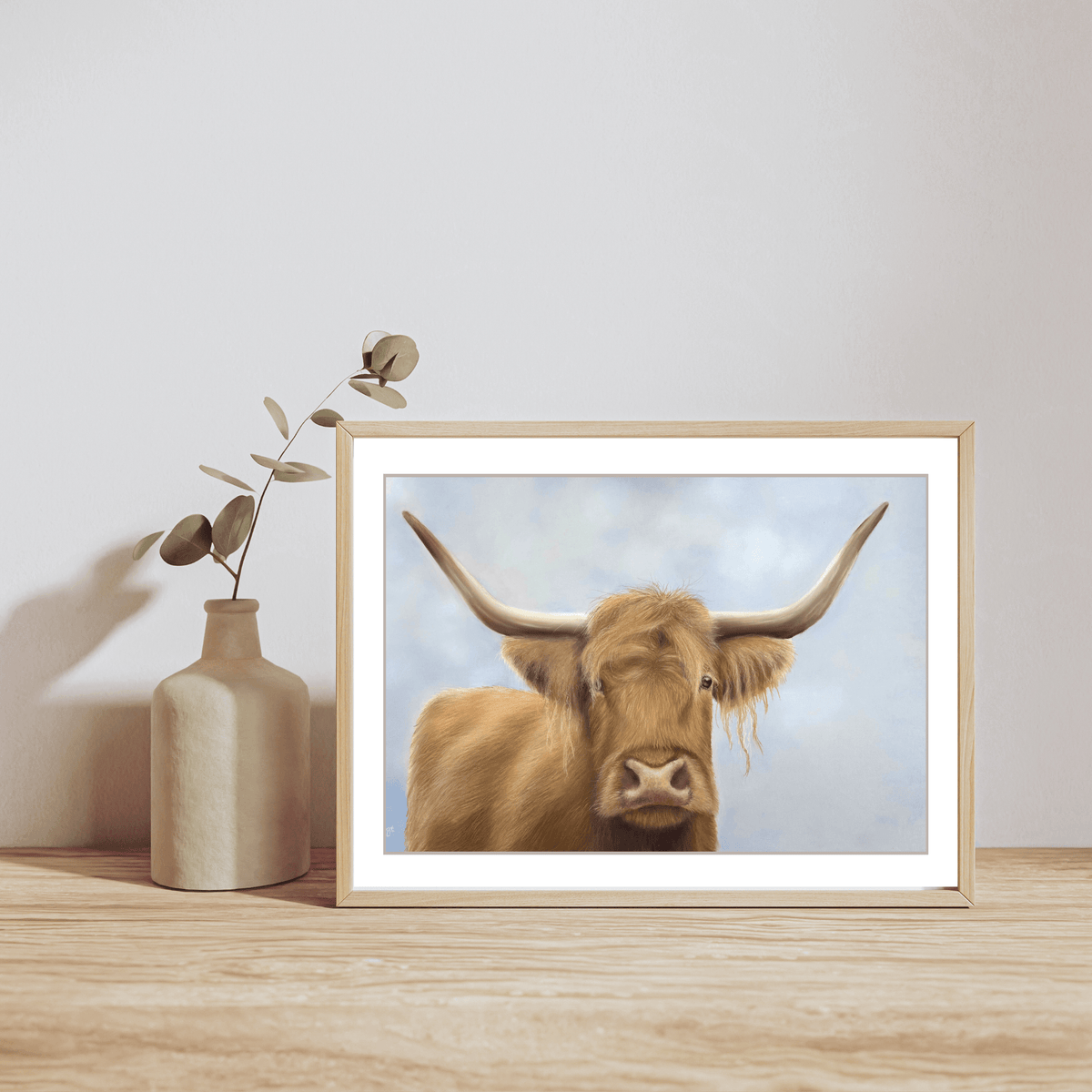 Scottish Highland Cow Print displayed in a light wood frame on a wooden surface with minimalist vase. Perfect fine art print for country-themed decor.