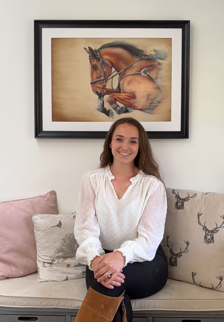 Woman sitting on a couch with a framed painting of a horse on the wall behind her.