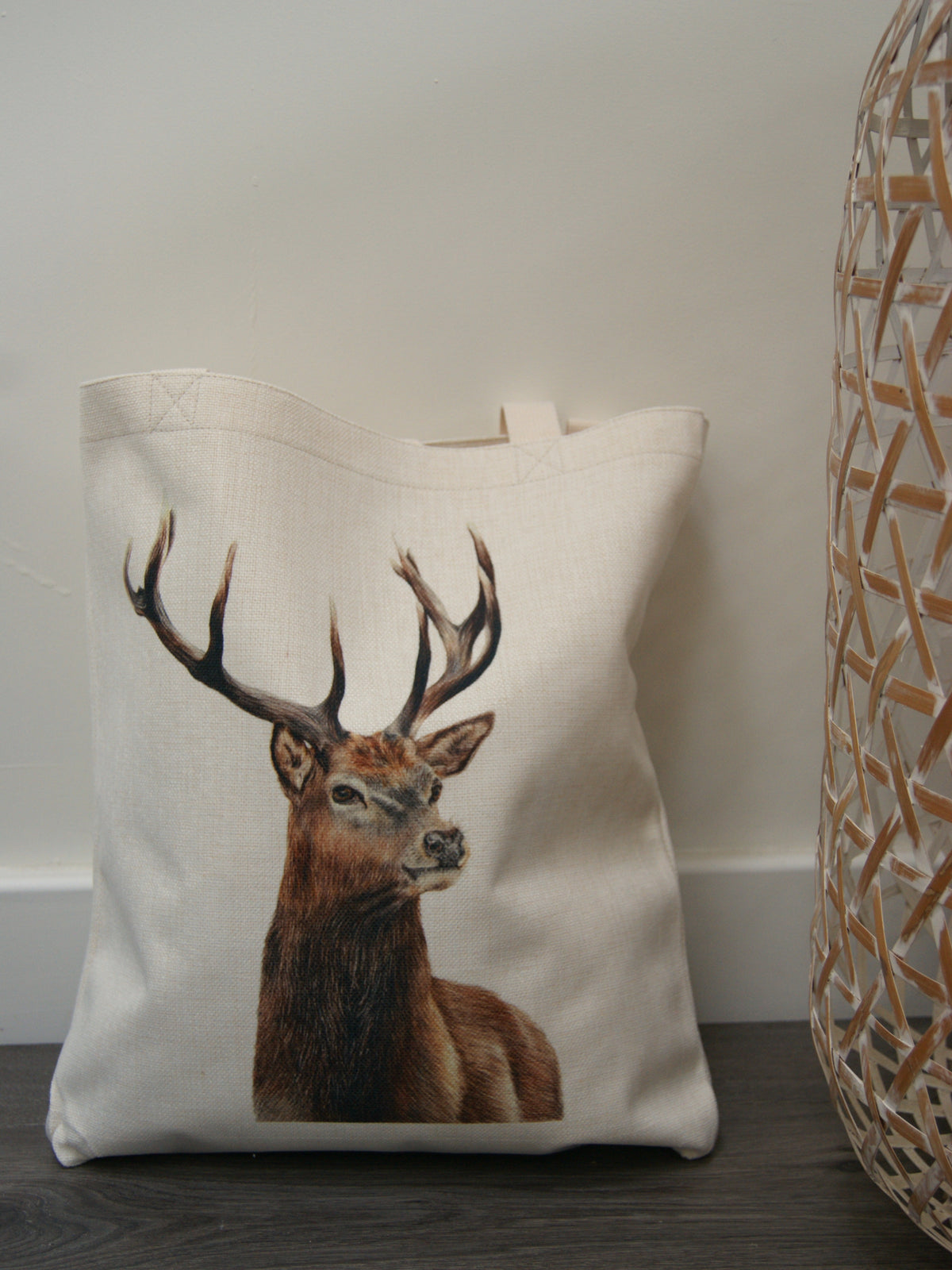 Eco-friendly stag tote bag with detailed stag illustration, placed on the floor beside a wicker basket. Reusable linen bag for shopping or gifting.