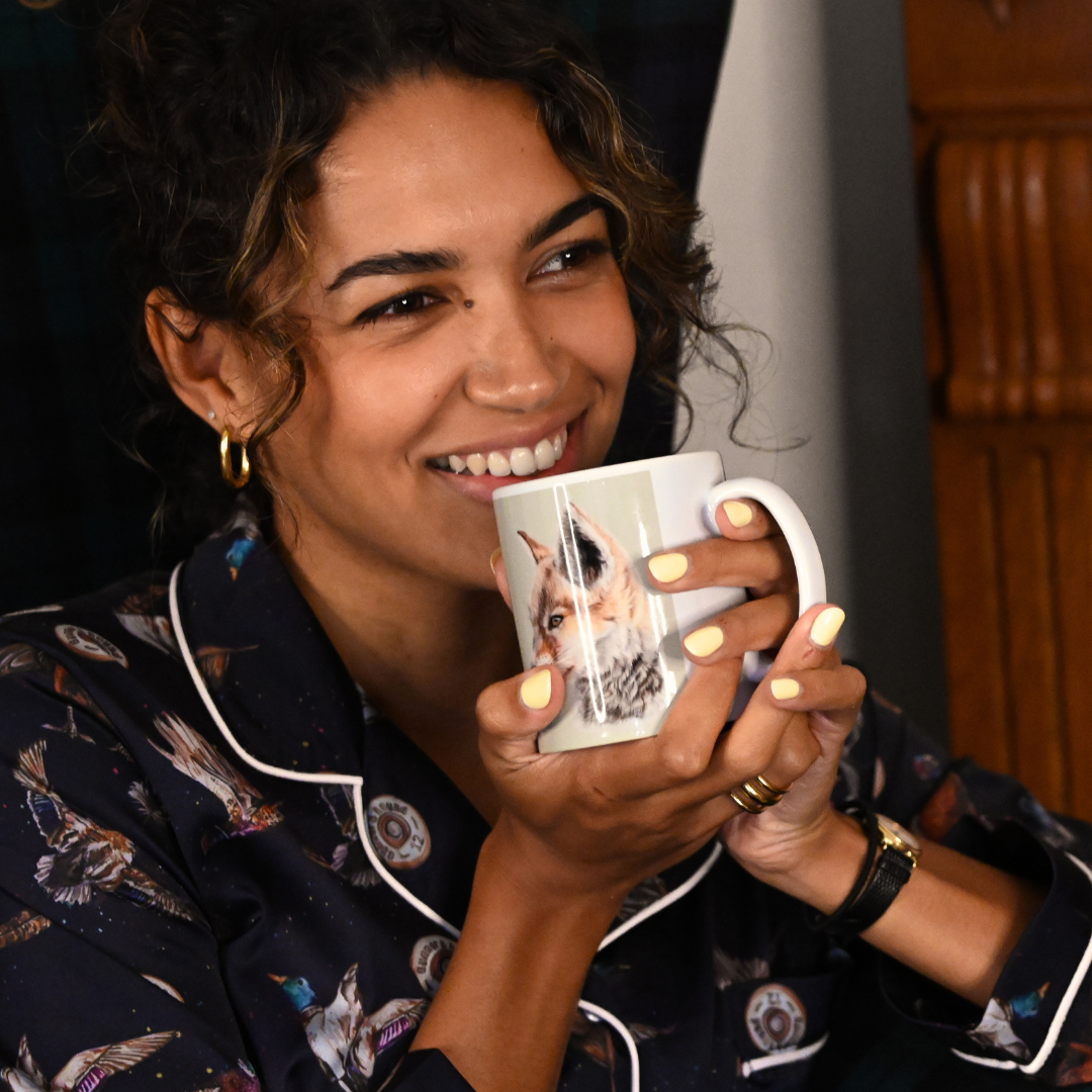 Woman in pyjamas holding a mug with a fox design, smiling.