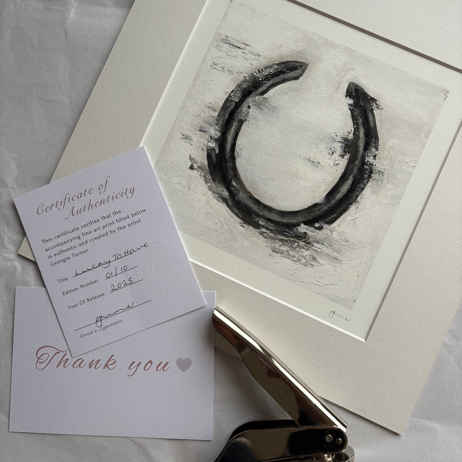 Framed artwork of a horseshoe with a paper clip and stationery items on a white background