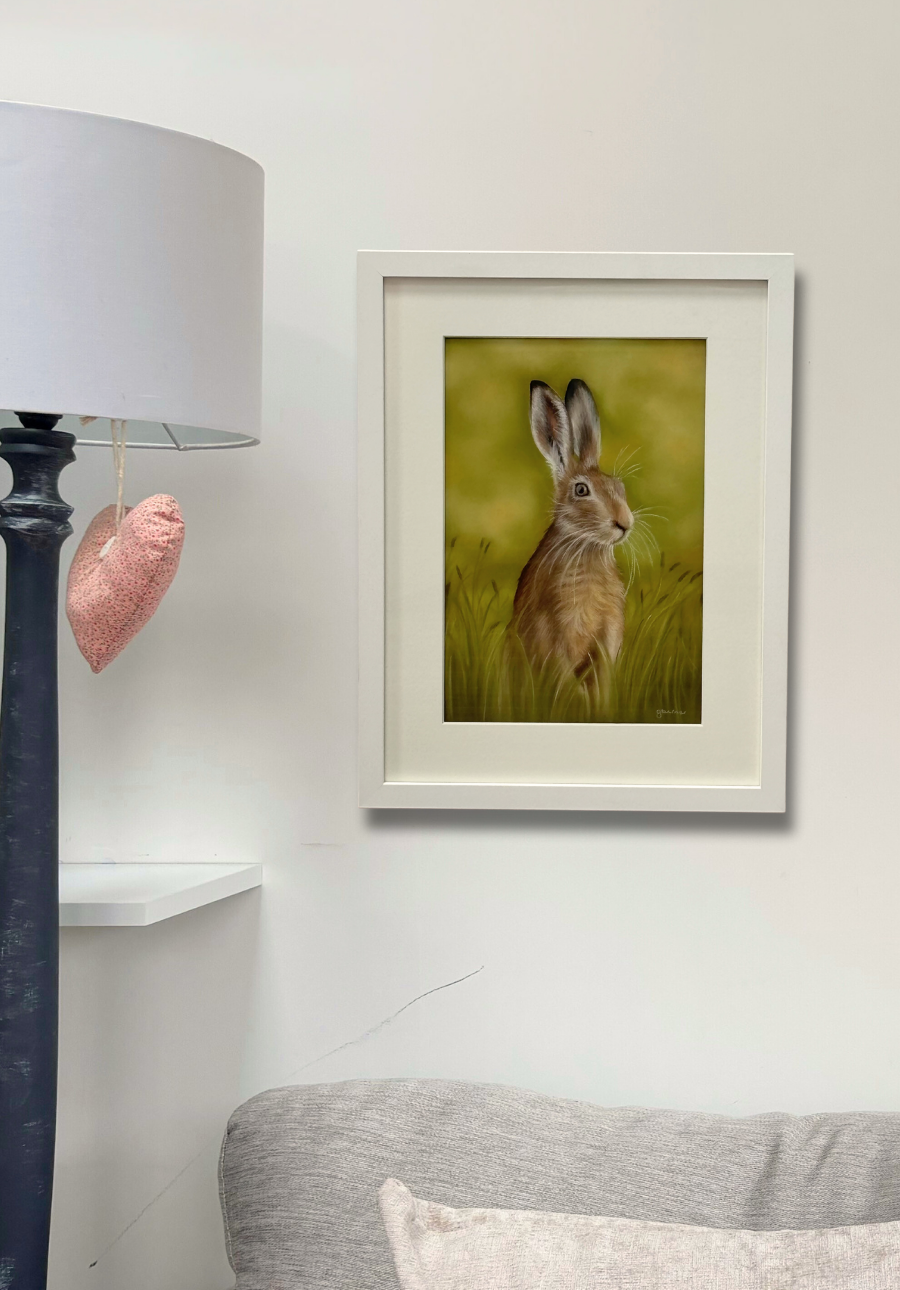 'Hare In The Grass' framed original artwork by Georgie Turner hung above a sofa. Elegant country home decor for living room wall display.