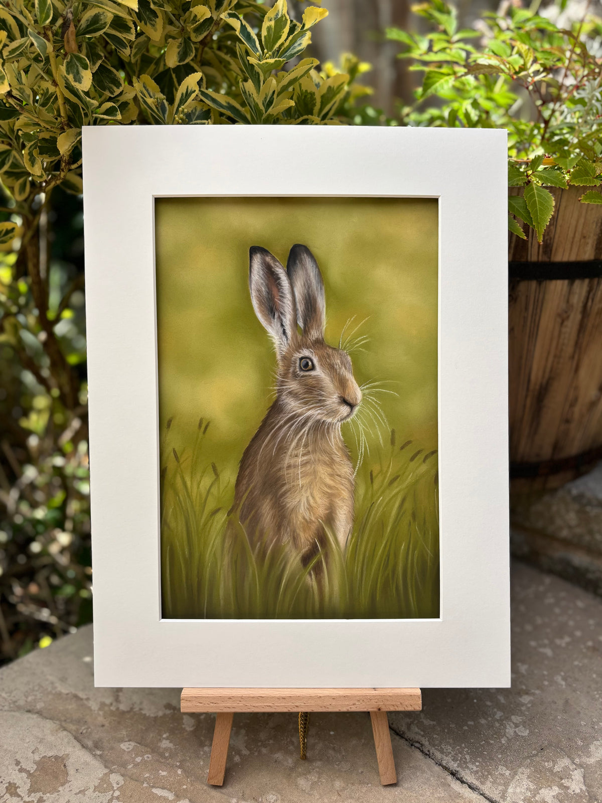 'Hare In The Grass' original painting by Georgie Turner on easel in garden. Country-themed wall art for rustic and nature-inspired interiors.