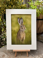 'Hare In The Grass' original painting by Georgie Turner on easel in garden. Country-themed wall art for rustic and nature-inspired interiors.