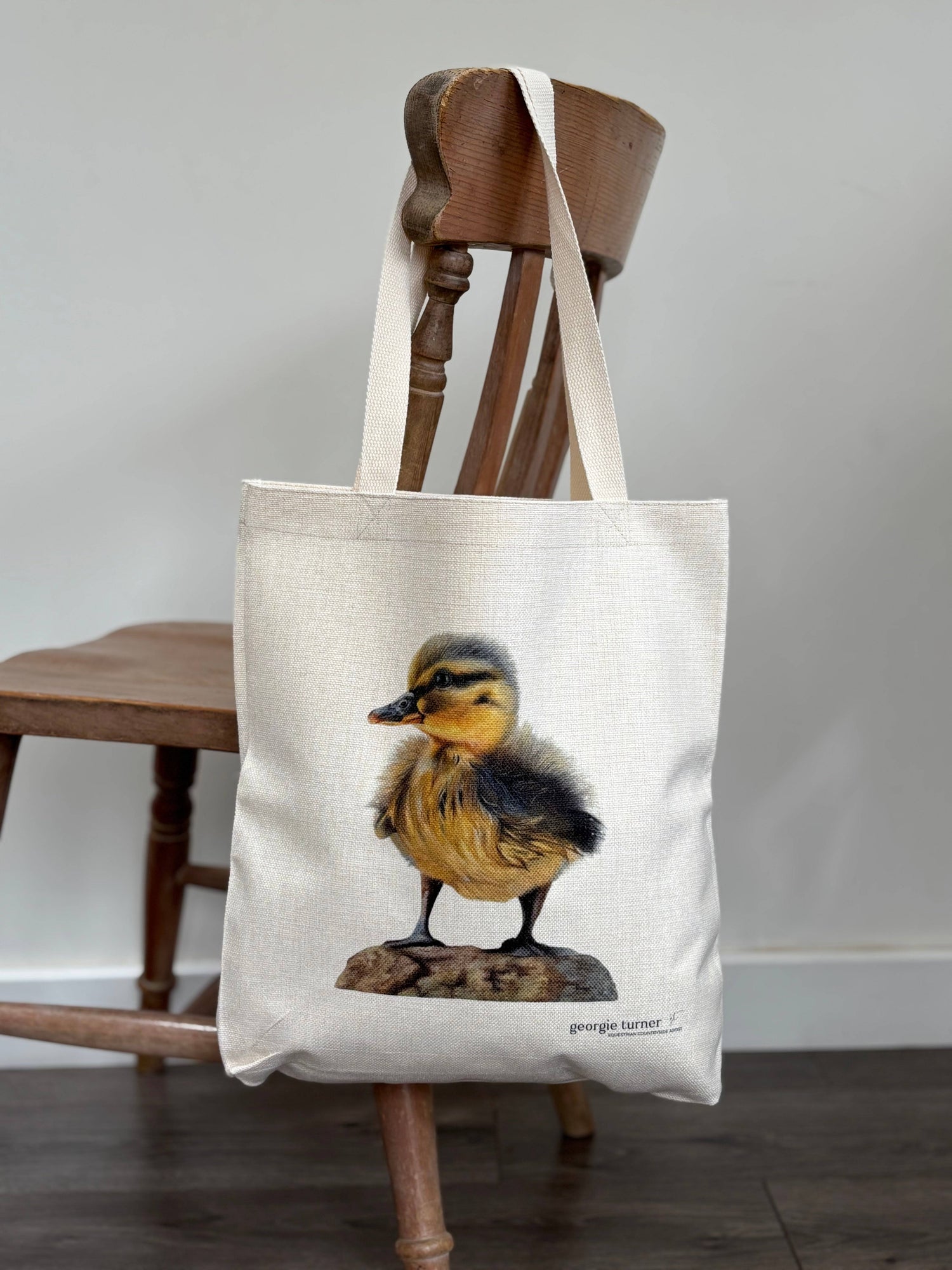 Eco-friendly duck tote bag hanging on a wooden chair, showcasing detailed duckling print. Stylish and sustainable tote bag for women.