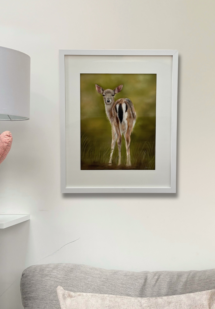 Framed artwork of a deer in a grassy field on a wall above a sofa.