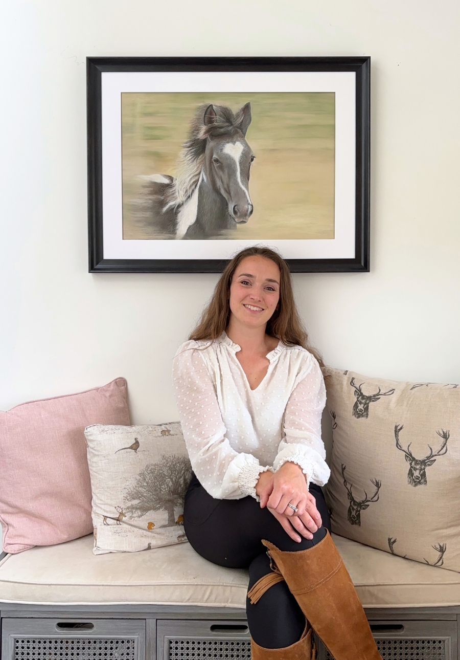 Equestrian original painting 'Flying Free' by Georgie Turner shown framed above a bench with a woman seated, perfect for rustic interior styling.