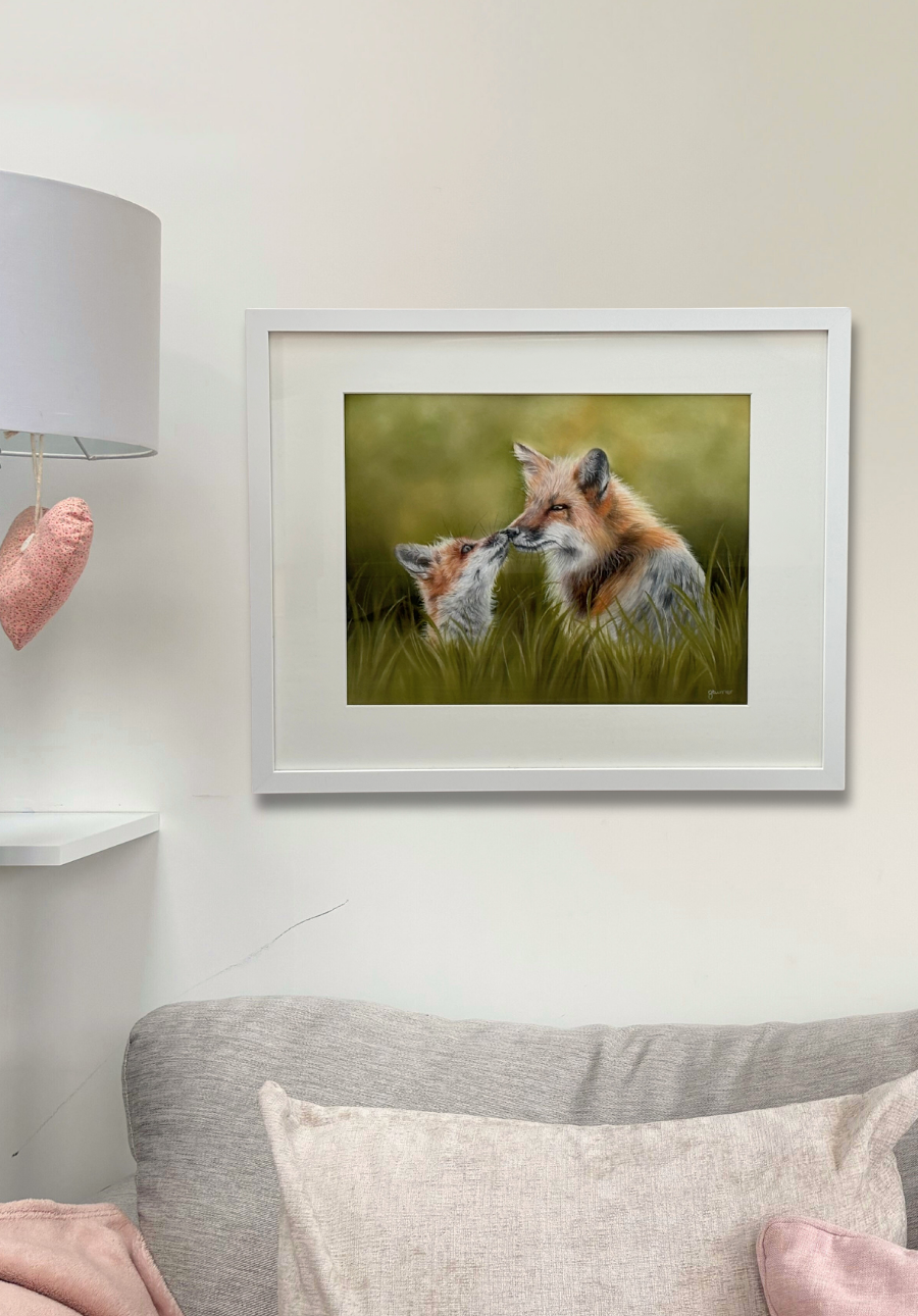 Framed artwork of two foxes kissing on a wall above a sofa.