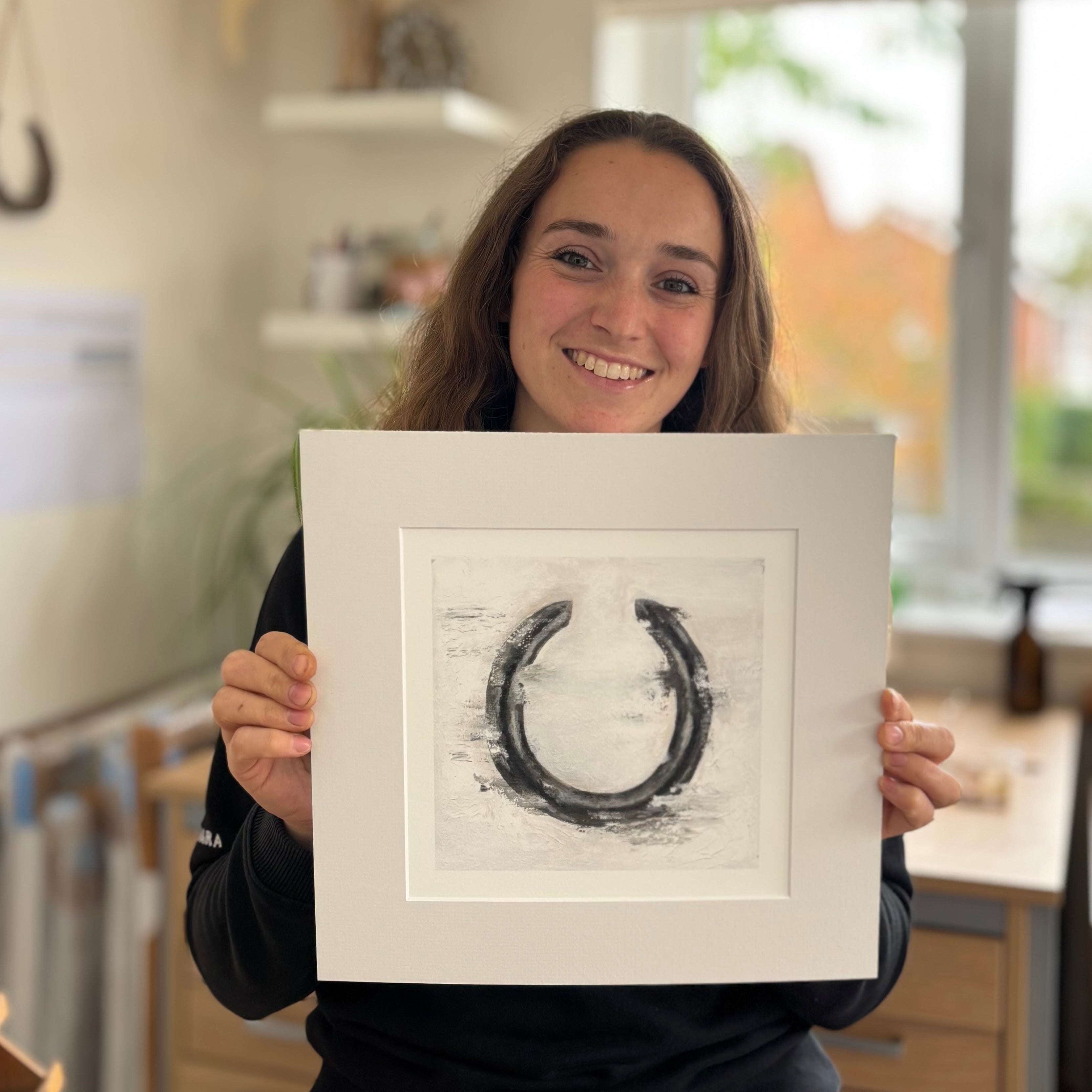 Person holding a framed artwork of a horseshoe in a kitchen setting