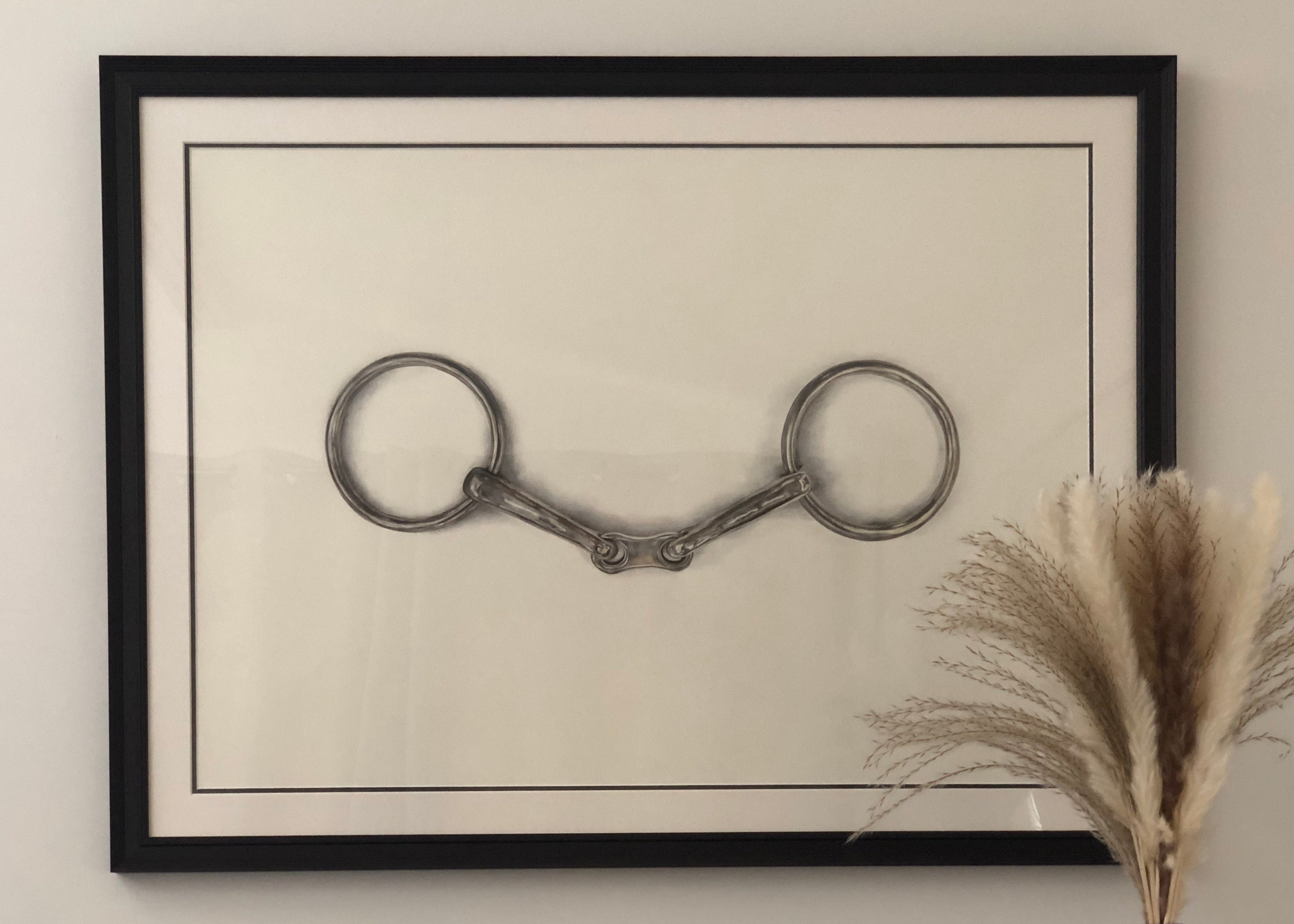 Framed artwork of a horse bridle on a beige wall with a decorative plant.
