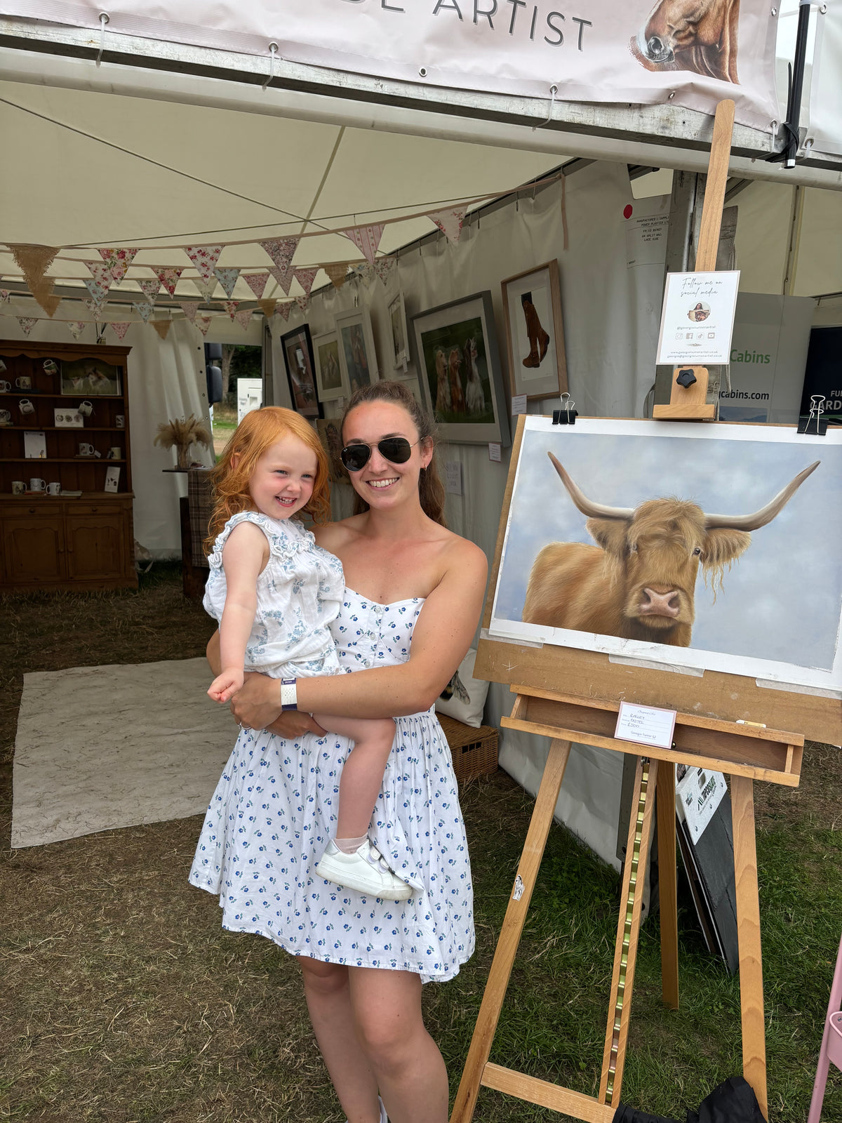 Mother and child at art fair with Scottish Highland Cow Wall Art | Original Pastel Painting on easel, perfect for country-style interiors.