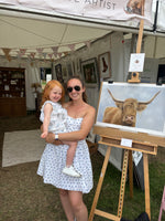 Mother and child at art fair with Scottish Highland Cow Wall Art | Original Pastel Painting on easel, perfect for country-style interiors.