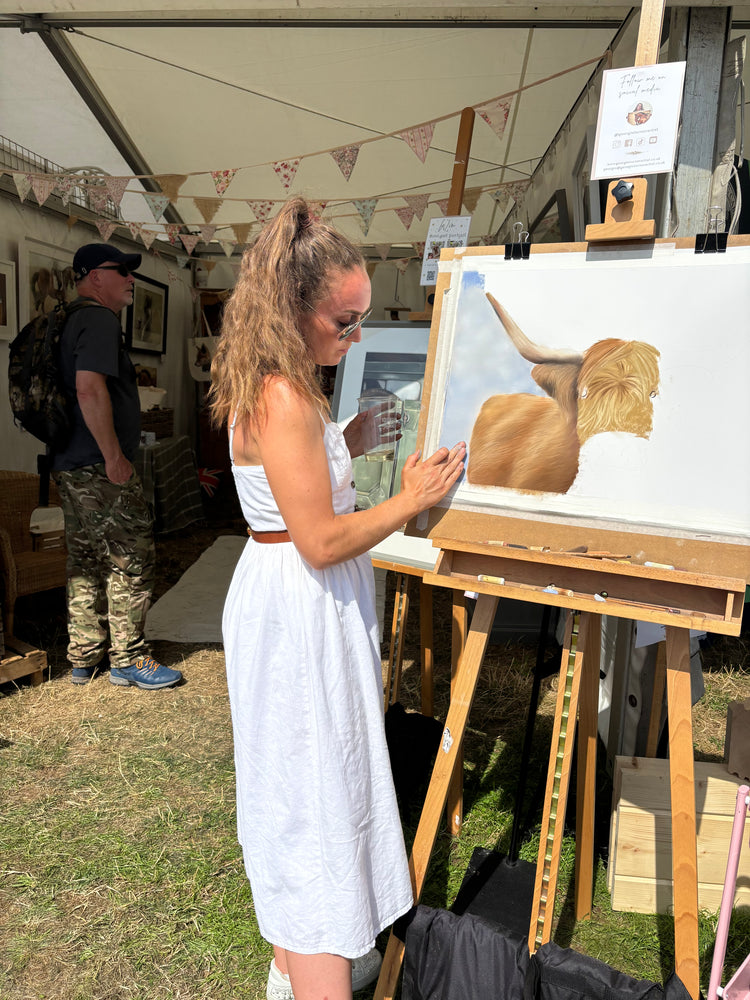 Georgie Turner painting a highland cow at The Game Fair 2025