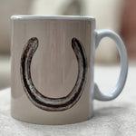 White mug with a black horseshoe design on a light surface.