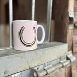 White mug with a horseshoe design on a metal surface