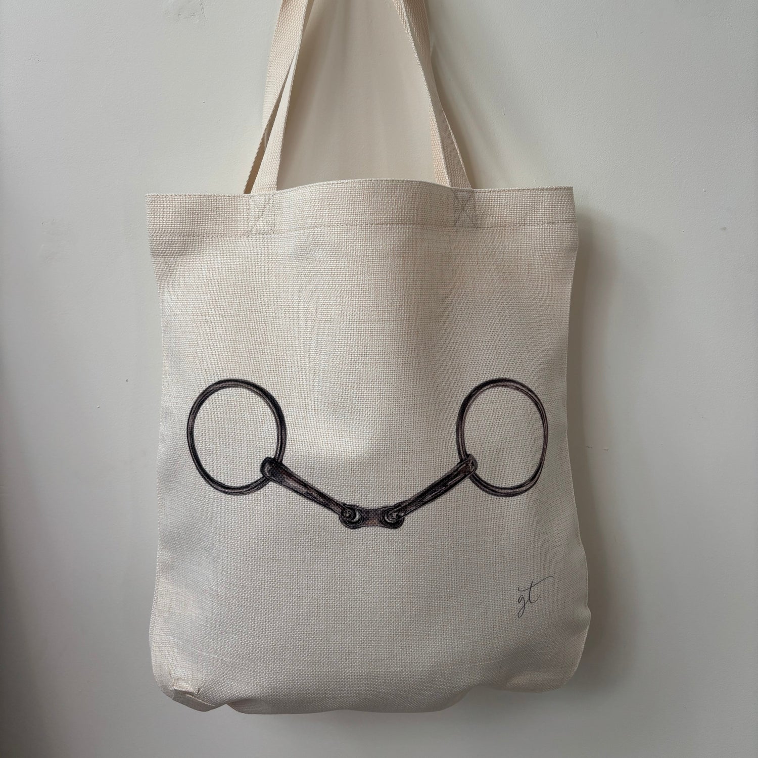 Beige tote bag with a black horse bridle design on a light gray background