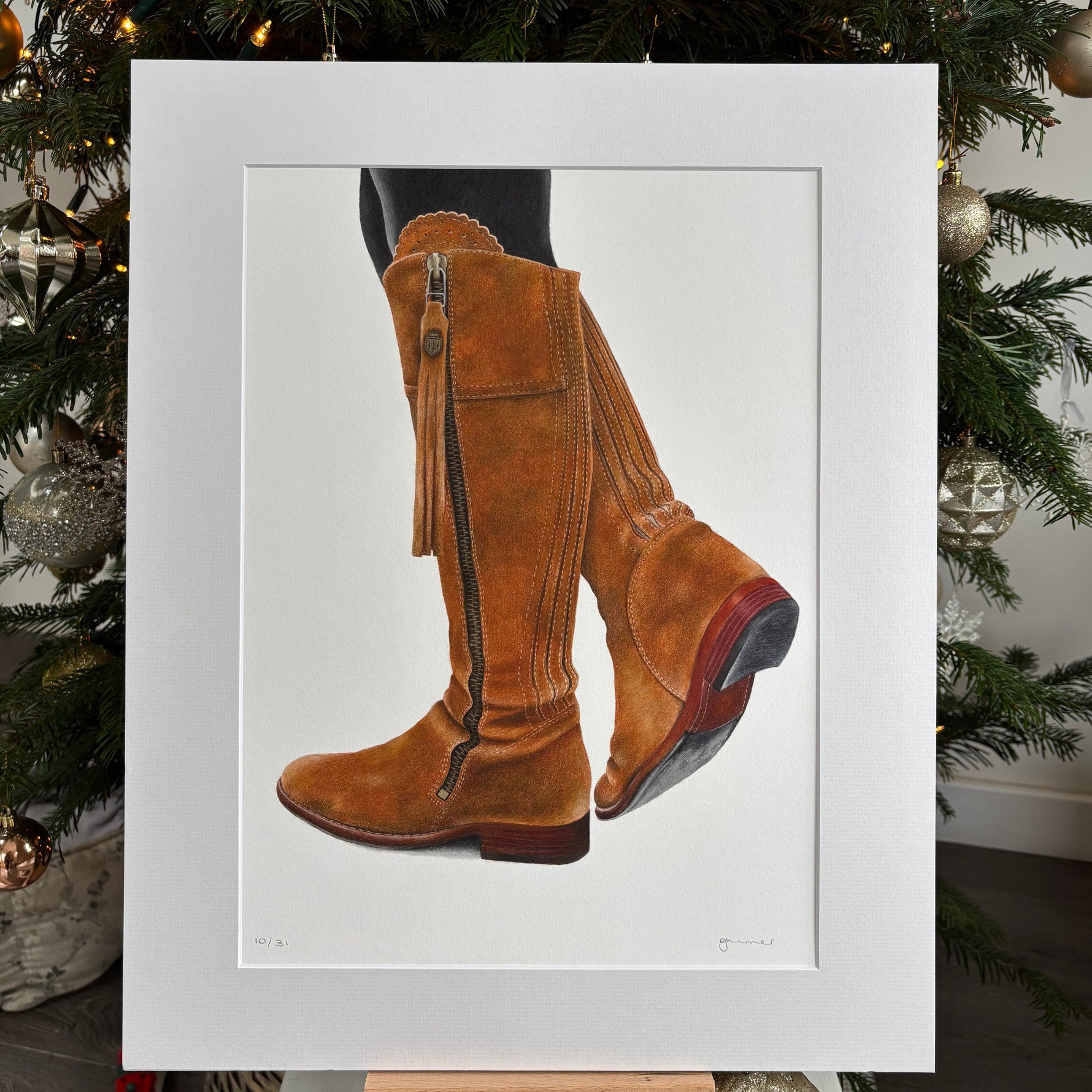 Framed picture of brown boots on a white background with a Christmas tree in the background