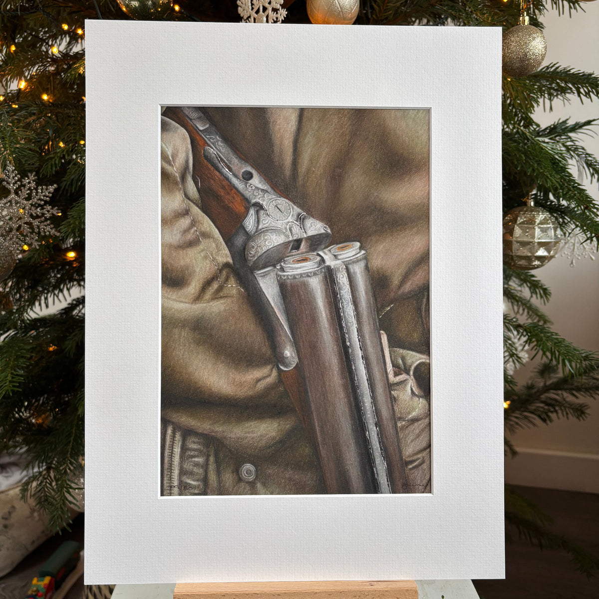 Framed picture of a rifle on a camouflage background with Christmas tree decorations.
