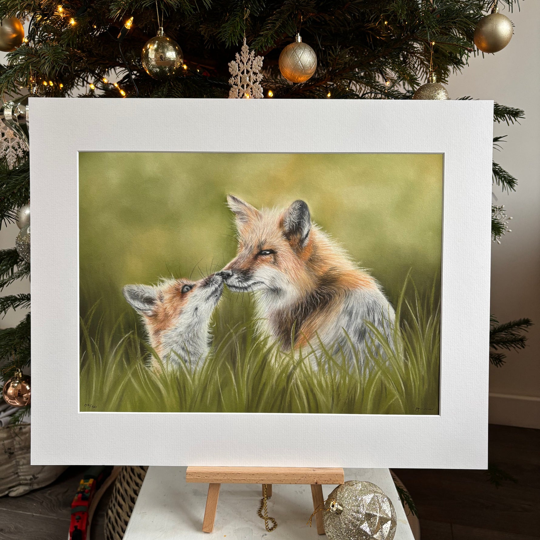 Framed artwork of two foxes on a Christmas tree with ornaments.